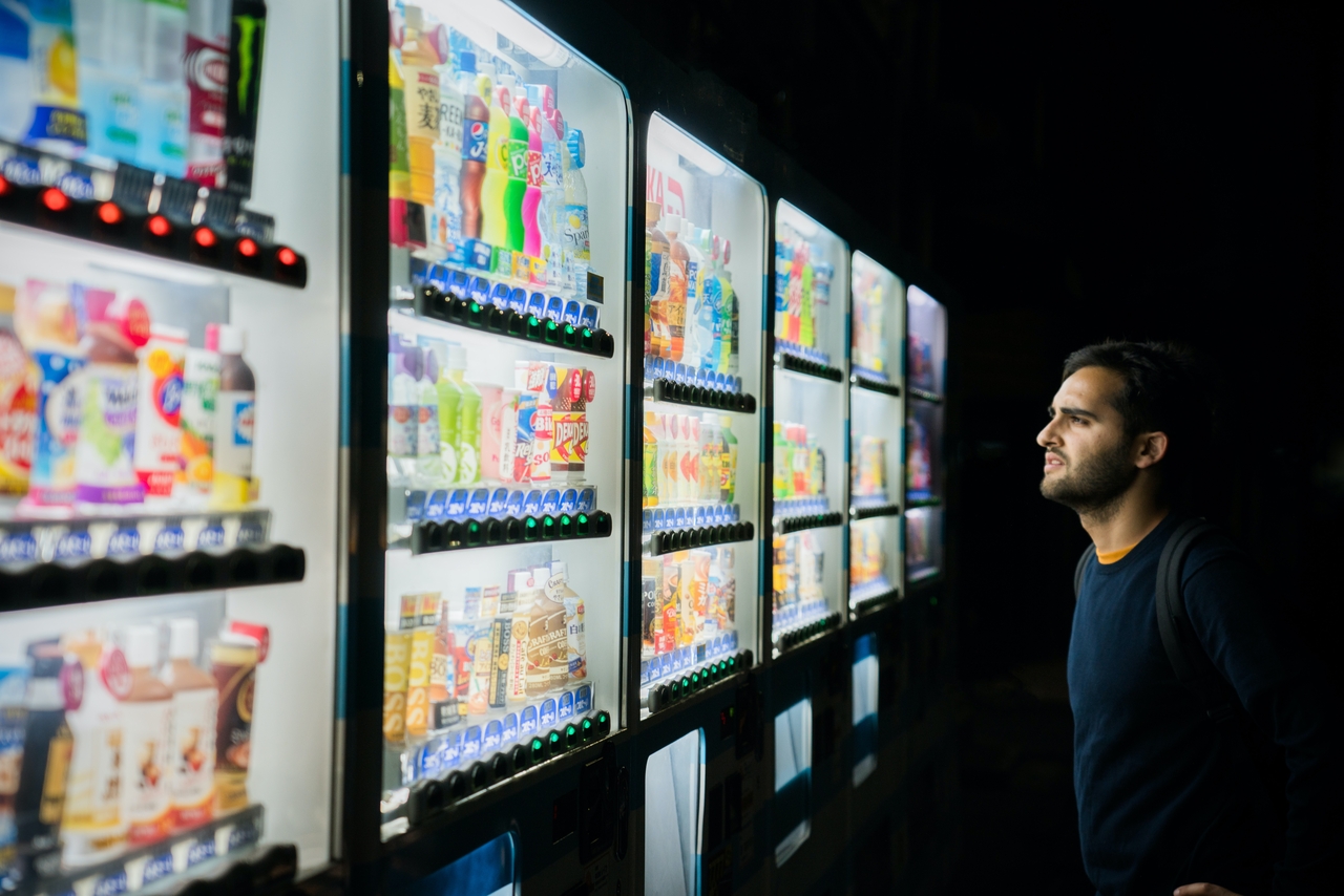 Person standing in front of a wall of vending machines, looking overwhelmed by the vast array of choices.