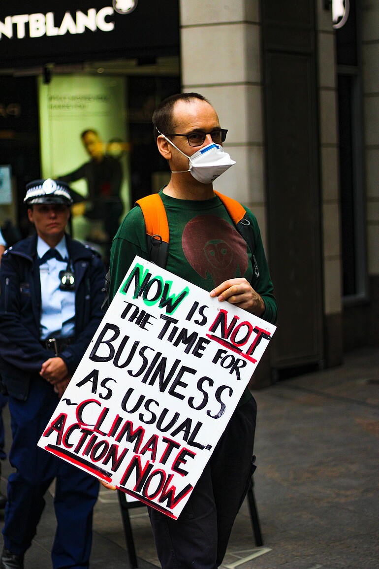 Photo shows an activist with poster saying climate action now