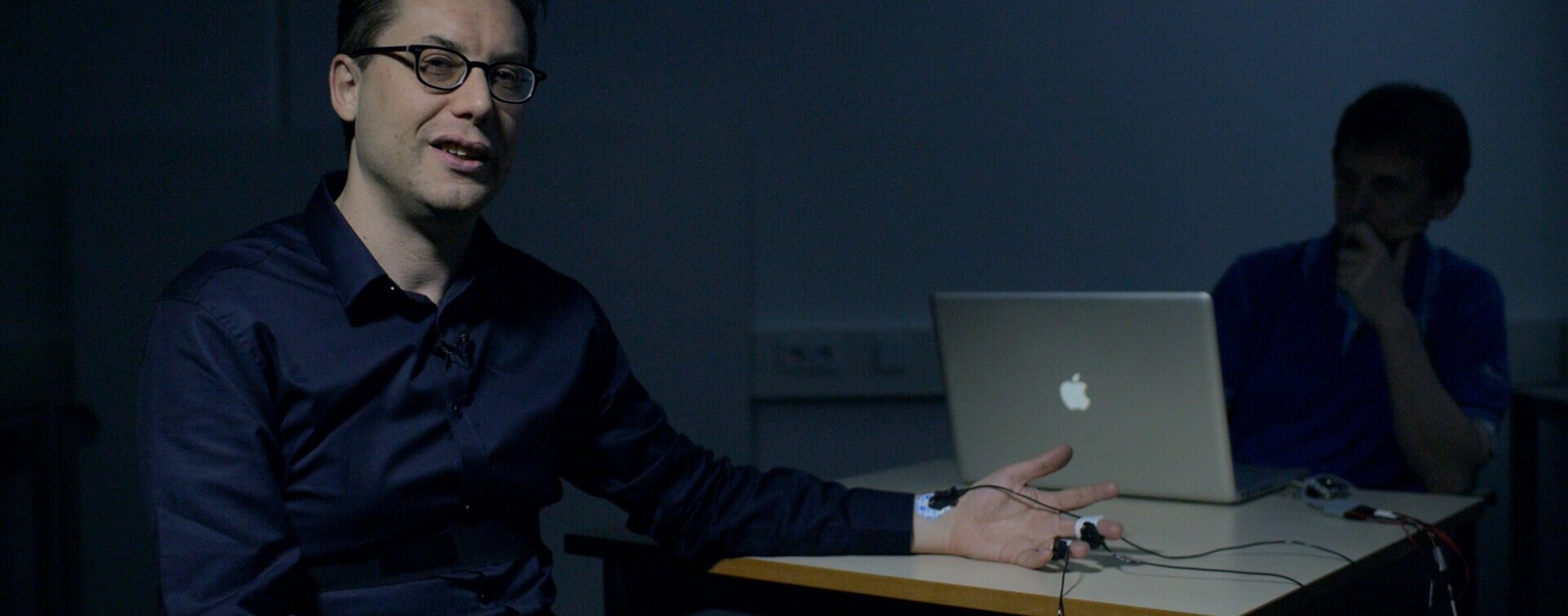 A man sitting in a dark room with a lie detector attached to him