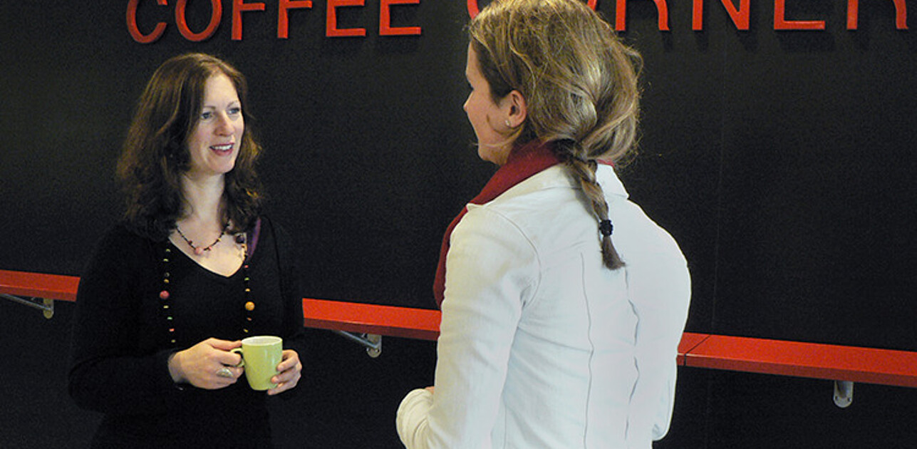 2 colleagues chatting with a cup of coffee in their hands