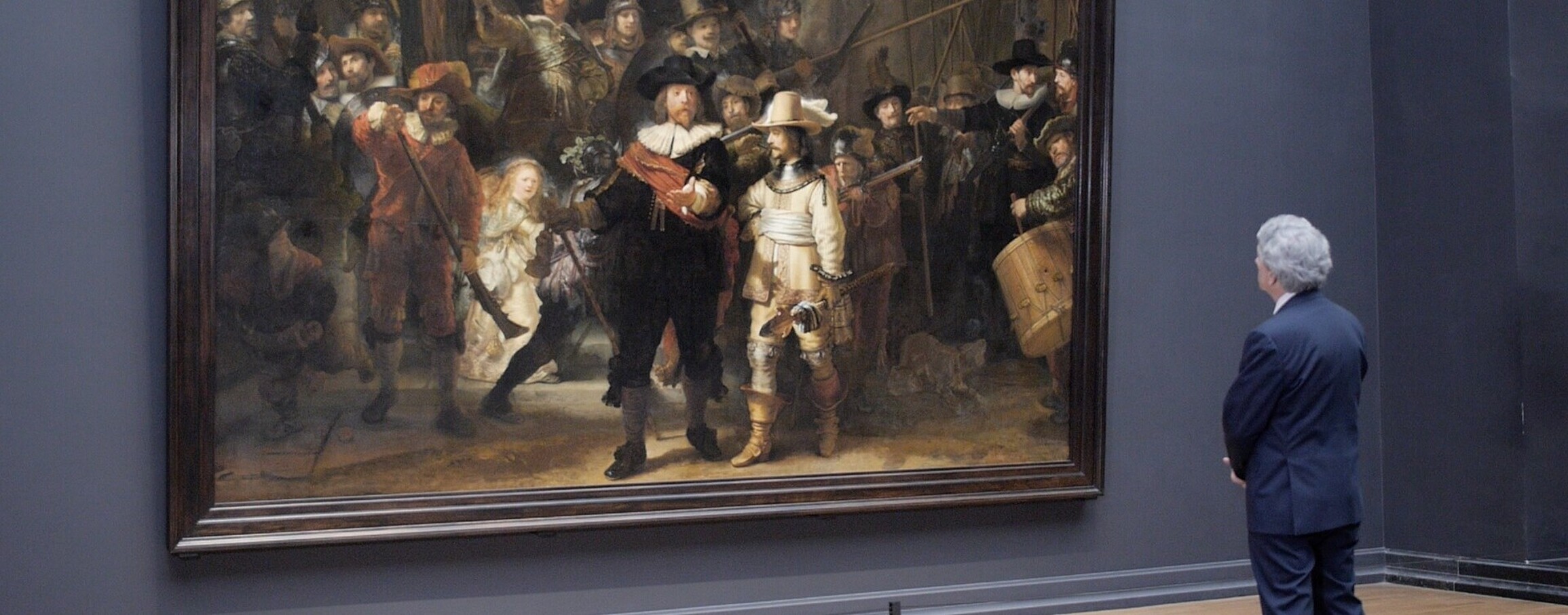 A man is looking at the dutch painting the "nachtwacht" created by Rembrandt van Rijn