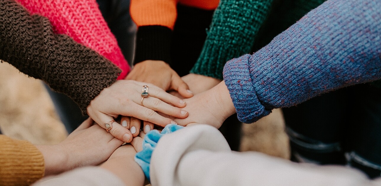 Image of a group of students standing in a circle, putting their hands together. The image represents the power of teamwork and collaboration to make positive change.