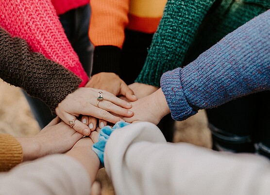 Image of a group of students standing in a circle, putting their hands together. The image represents the power of teamwork and collaboration to make positive change.