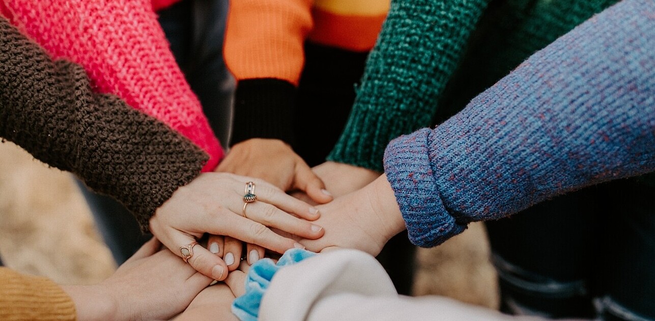 Image of a group of students standing in a circle, putting their hands together. The image represents the power of teamwork and collaboration to make positive change.