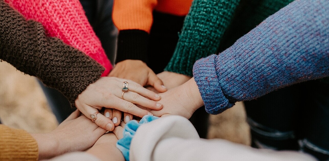 Image of a group of students standing in a circle, putting their hands together. The image represents the power of teamwork and collaboration to make positive change.