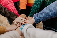 Image of a group of students standing in a circle, putting their hands together. The image represents the power of teamwork and collaboration to make positive change.