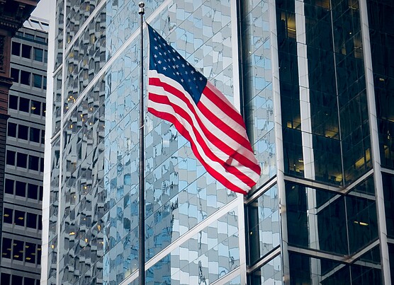 An American flag flying in front of glass office towers in a US business district, illustrating how US elections affect companies and stock markets.