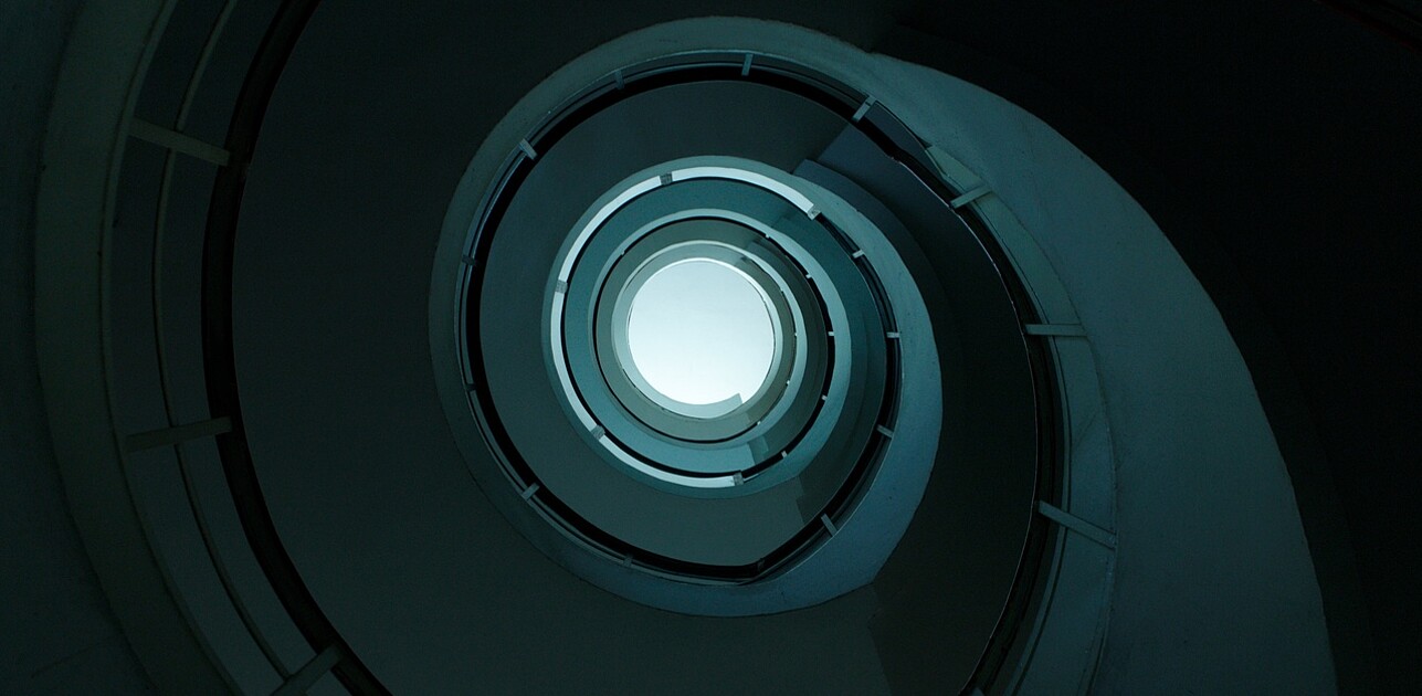 Spiraling multi-level parking garage with a central open void, offering a clear view of the sky through its circular opening.