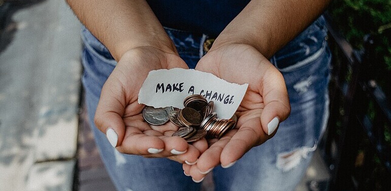 Two hands holding up change and a piece of paper stating "Make a change".