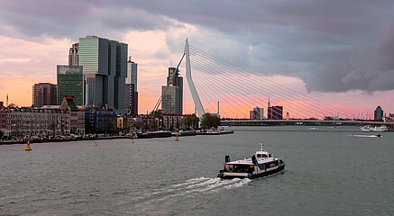 A boat sails through Rotterdam at sunset