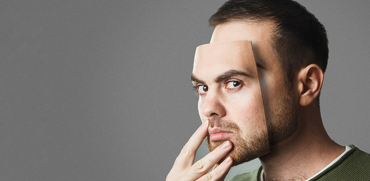 Man hiding his face with a mask that replicates his own facial features.