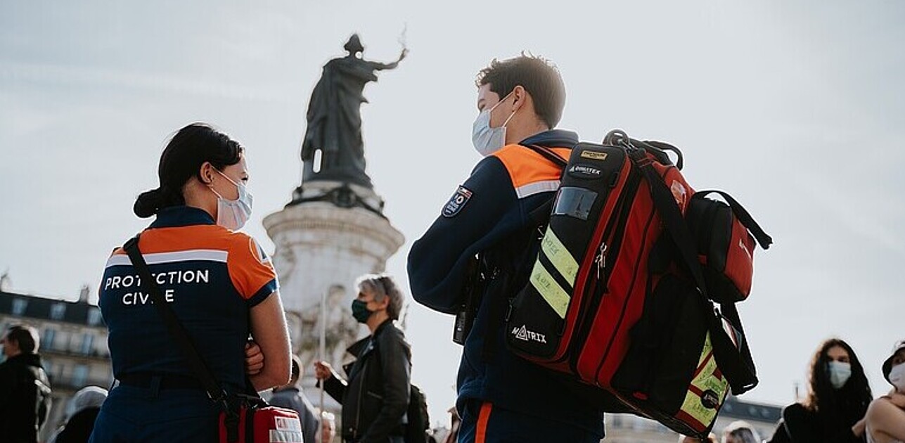 Photo shows two paramedics on a public space in front of a statue