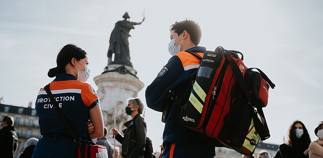 Photo shows two paramedics on a public space in front of a statue