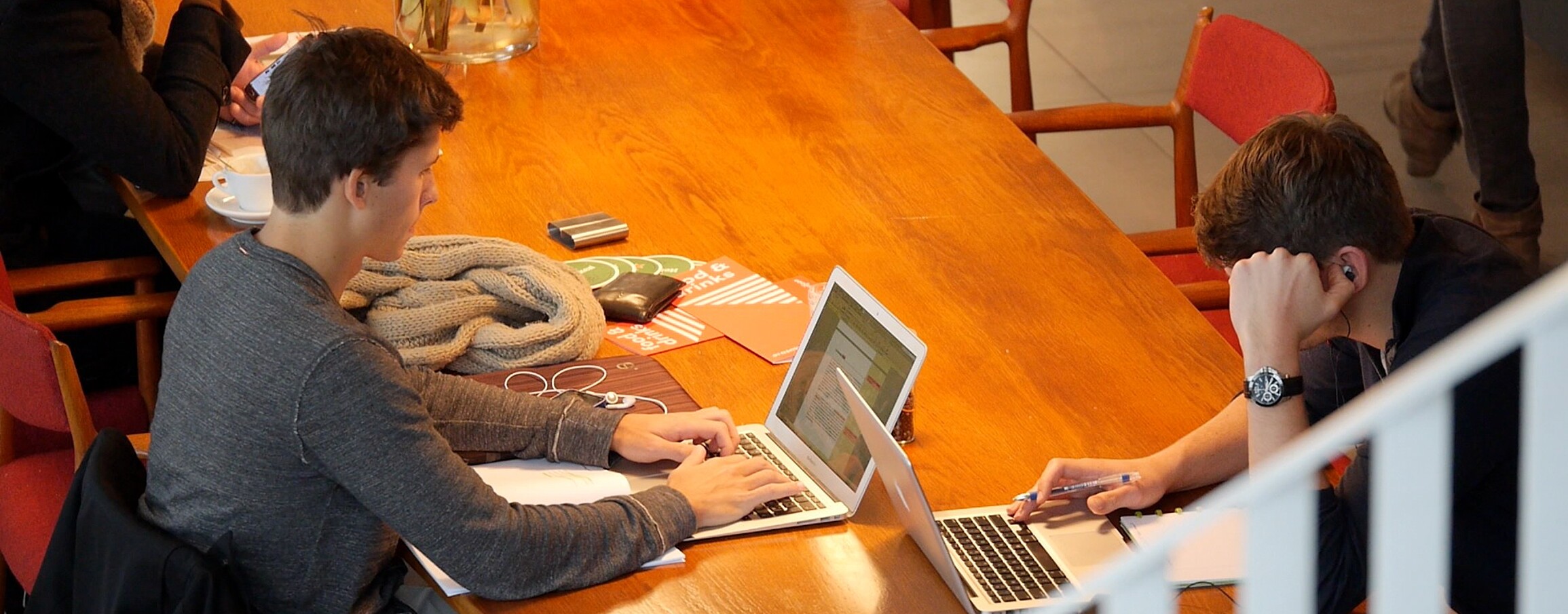 Students seated at a cafe, engrossed in their studies, with laptops open in front of them.