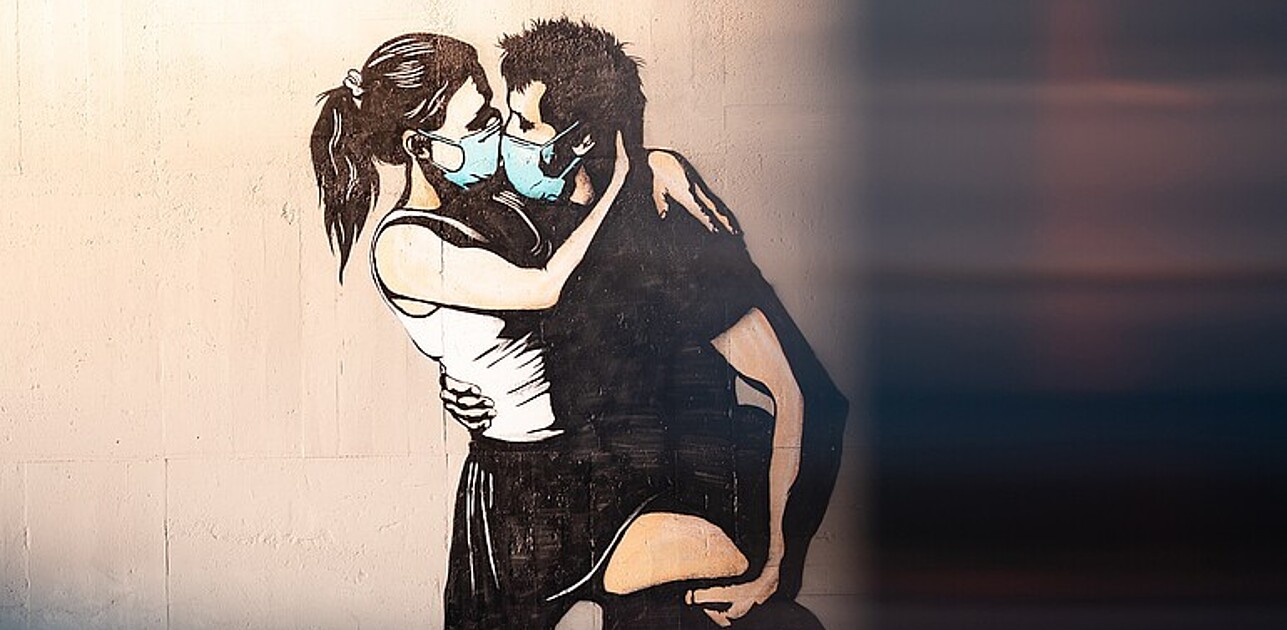 Grafitti of kissing people wearing masks.