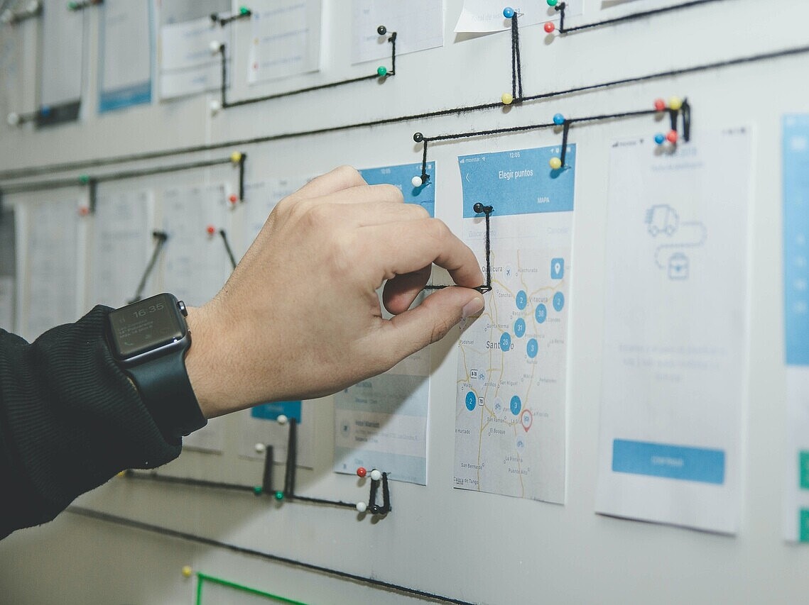 Hand connecting various notes on a whiteboard using a wire, illustrating interconnected management strategies and planning.