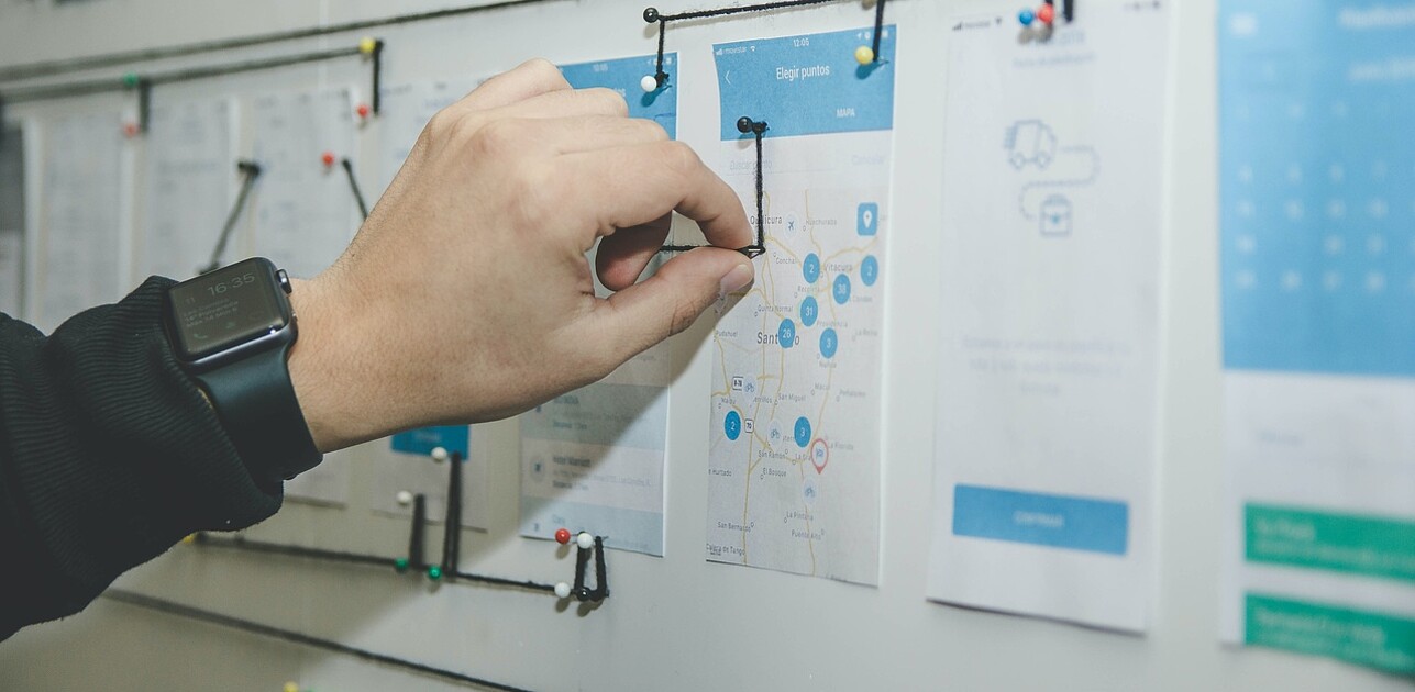 Hand connecting various notes on a whiteboard using a wire, illustrating interconnected management strategies and planning.