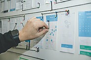 Hand connecting various notes on a whiteboard using a wire, illustrating interconnected management strategies and planning.