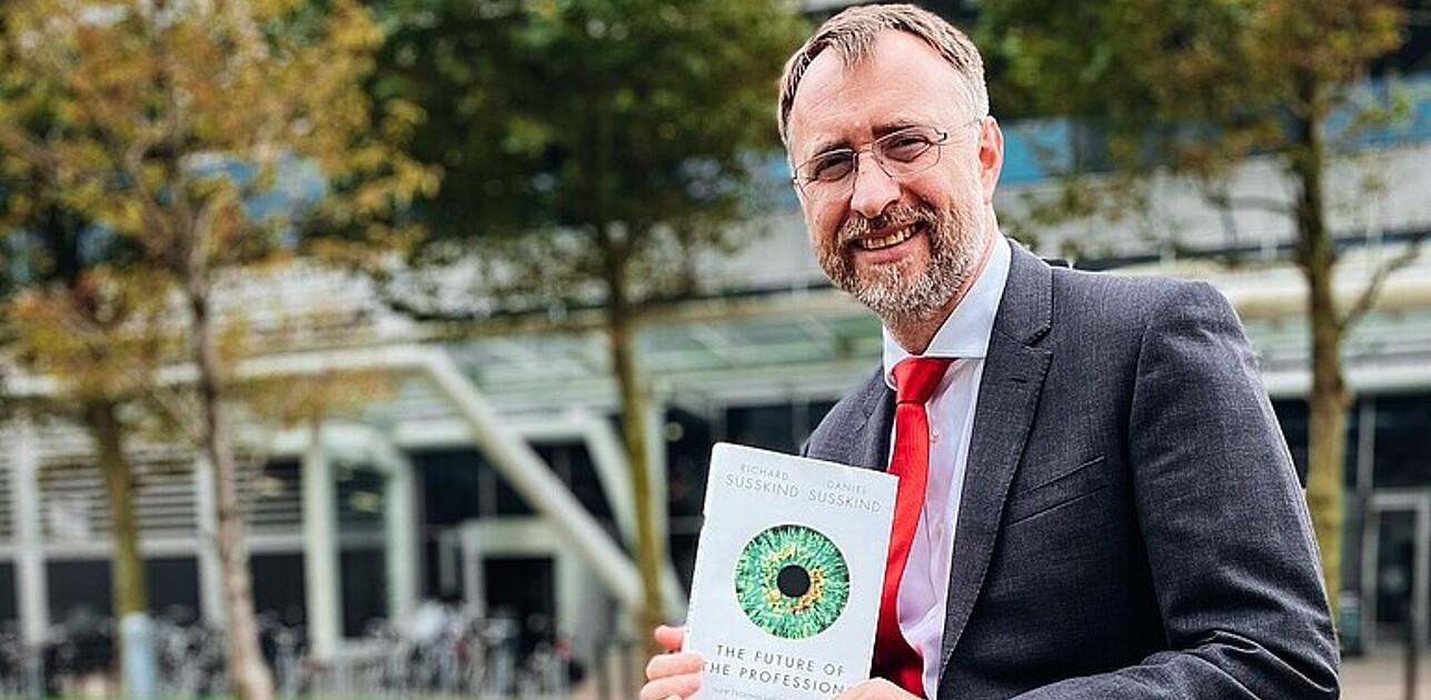 Dean Ansgar Richter sitting on a bench holding the book The future of the profession.