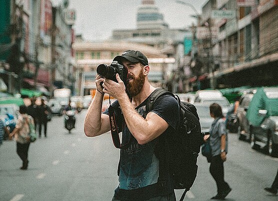 Photo shows a male photographer with a camera in a busy street.