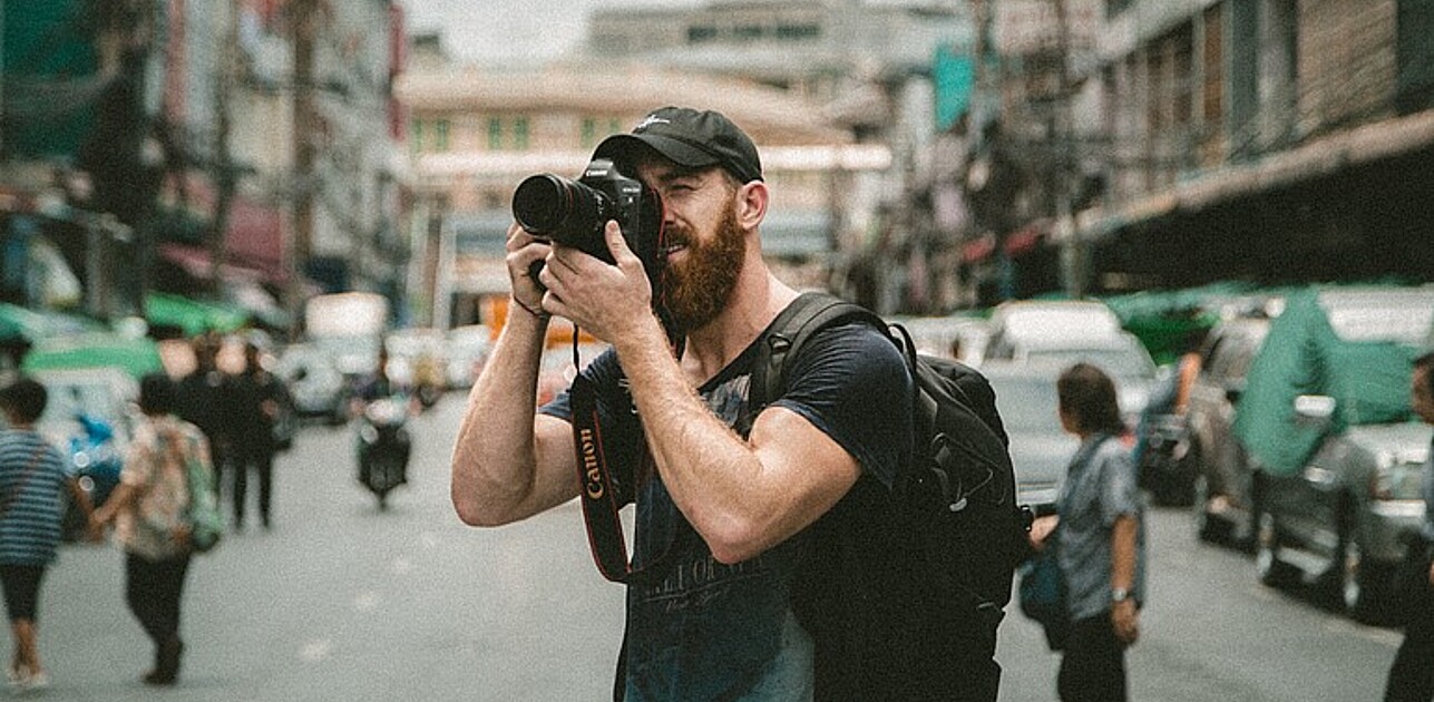 Photo shows a male photographer with a camera in a busy street.