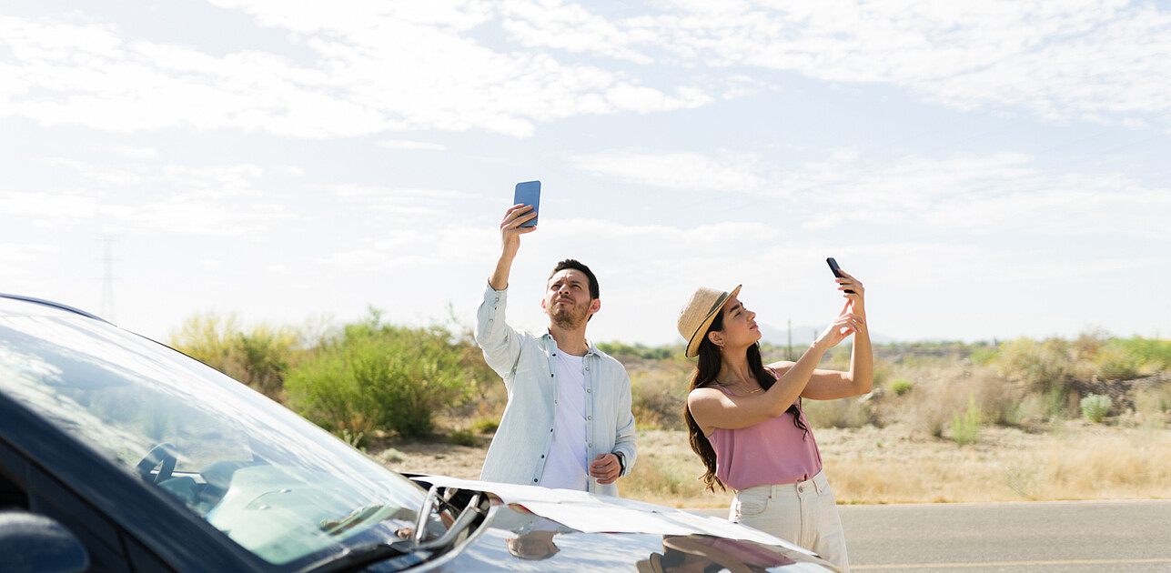 Couple standing on a road outside an urban area, both looking at their phones, searching for a signal.