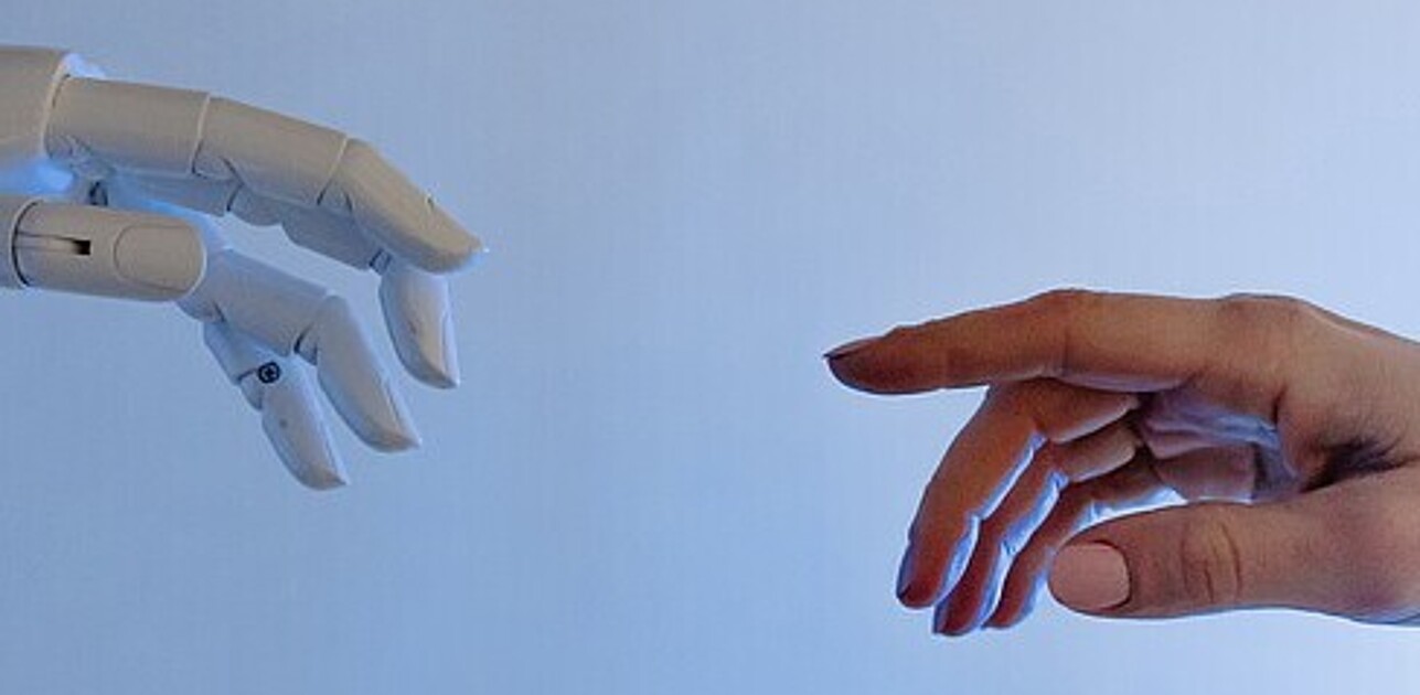 An image shows robotic hand and human hand about to touch