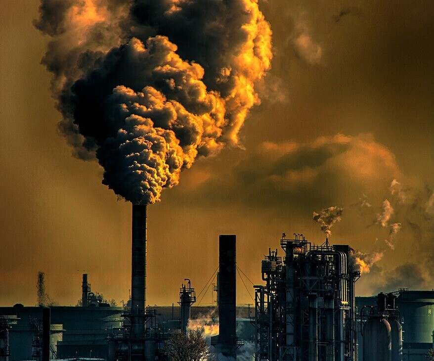 Industrial plant with tall smokestacks releasing dense smog into the atmosphere.