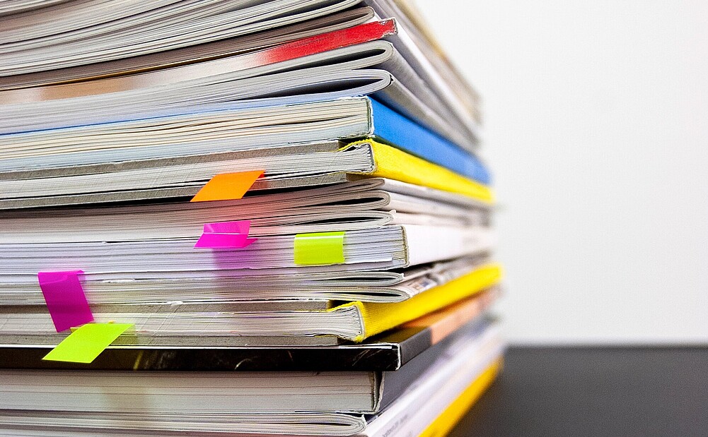 Pile of books with vibrant bookmarks protruding from various pages, symbolizing in-depth research.