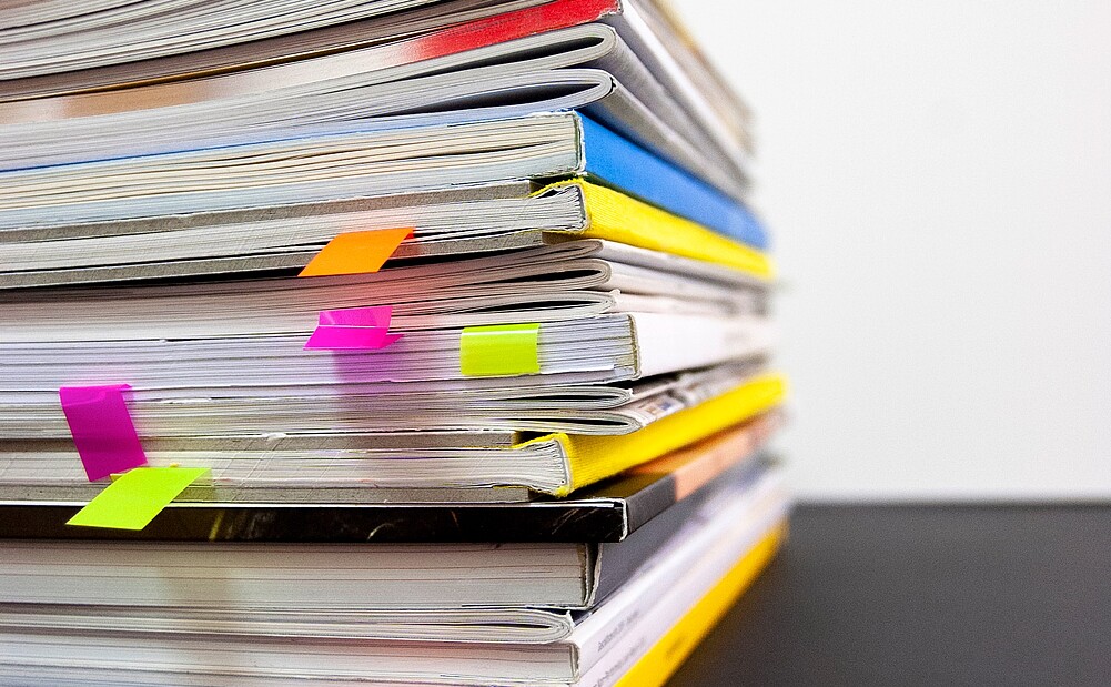 Pile of books with vibrant bookmarks protruding from various pages, symbolizing in-depth research.