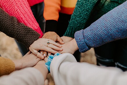 Image of a group of students standing in a circle, putting their hands together. The image represents the power of teamwork and collaboration to make positive change.
