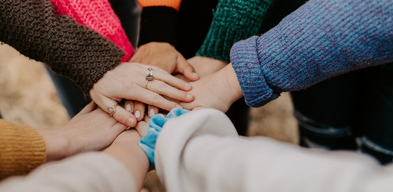 Image of a group of students standing in a circle, putting their hands together. The image represents the power of teamwork and collaboration to make positive change.