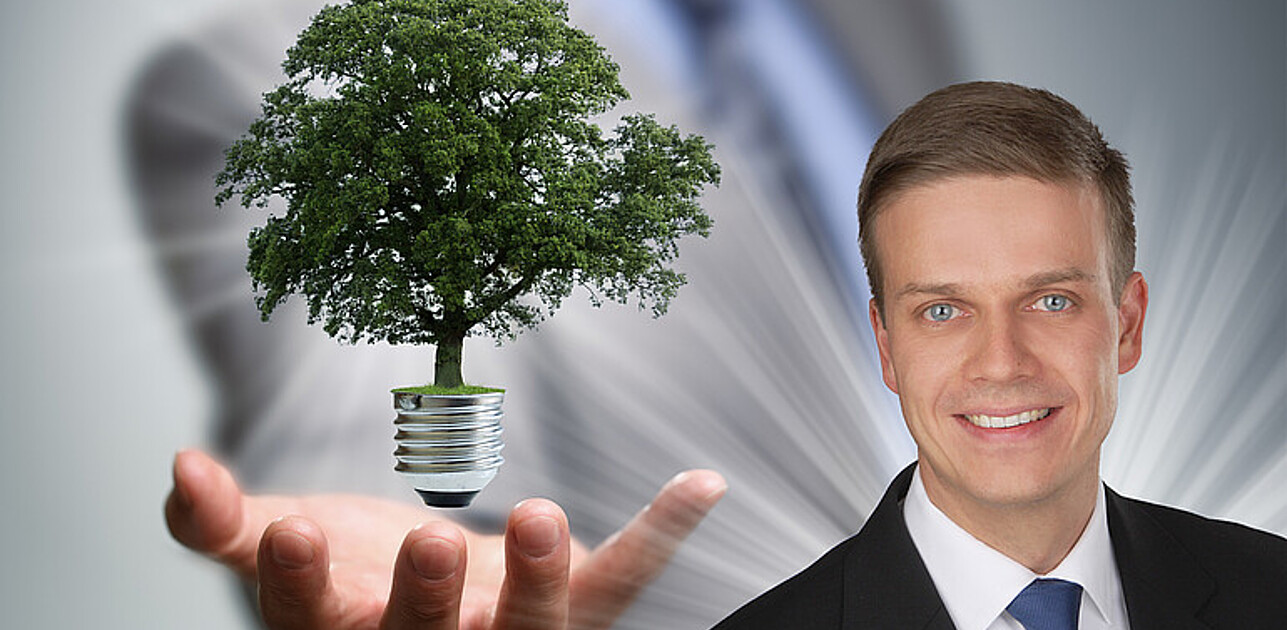 Man in a suit and tie holding a glowing, fluctuating lightbulb in the palm of his hand.