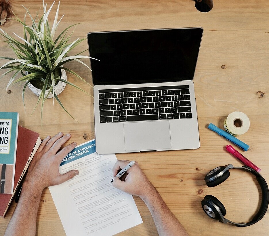 A plant, laptop, headphone and notepad layed down on a table