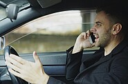 Frustrated driver talking on the phone inside a car, gesturing with his hand as if in a dispute.