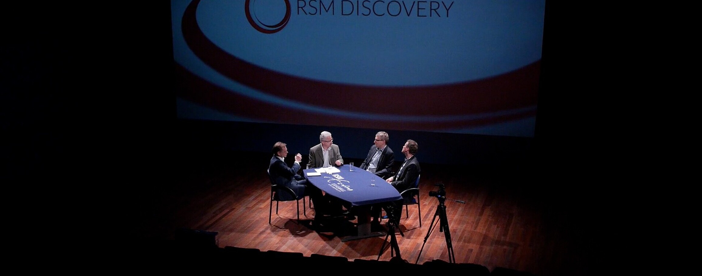 Four men debating whilst sitting by a table