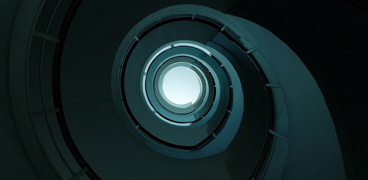 Spiraling multi-level parking garage with a central open void, offering a clear view of the sky through its circular opening.