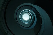 Spiraling multi-level parking garage with a central open void, offering a clear view of the sky through its circular opening.