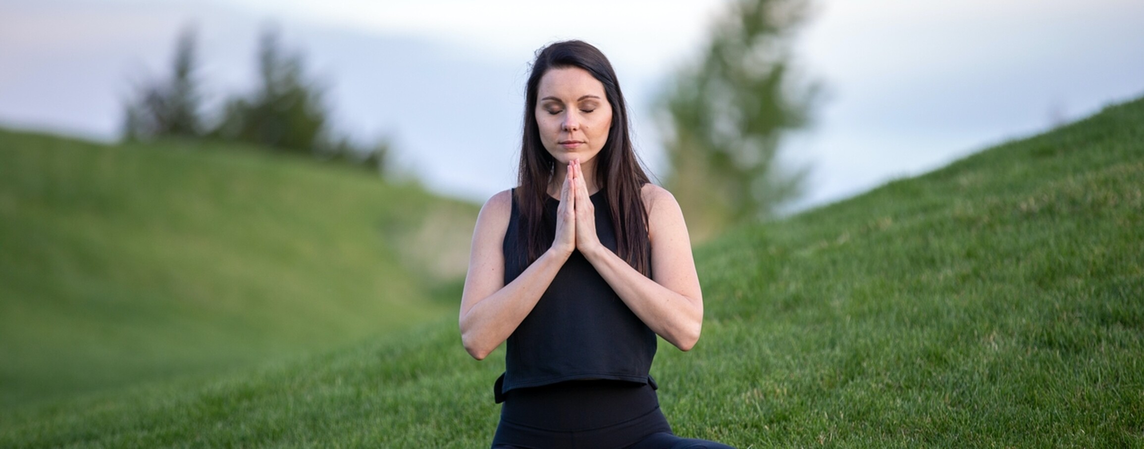 Woman meditating peacefully amidst rolling green hills.