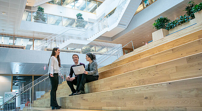 Master students sitting together on the stairs, one is standing