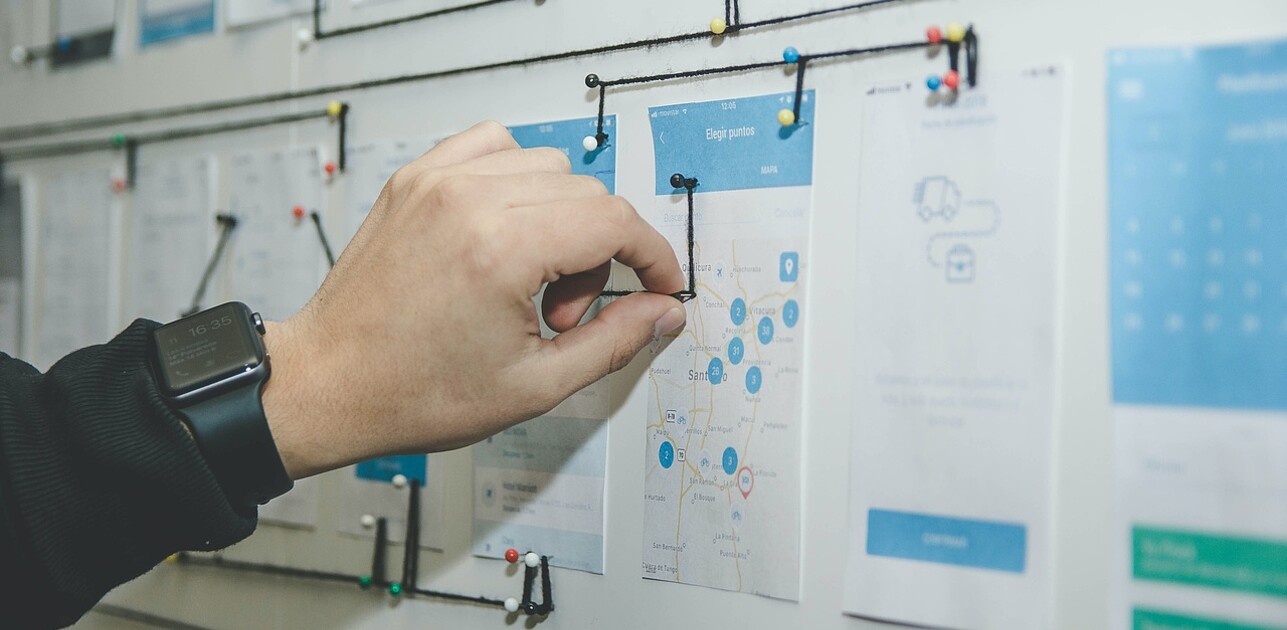 Hand connecting various notes on a whiteboard using a wire, illustrating interconnected management strategies and planning.