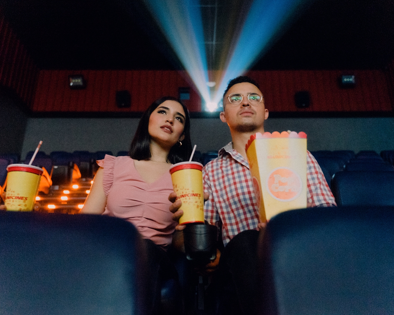 A photo shows man and woman eating popcorn in cinema while watching a movie