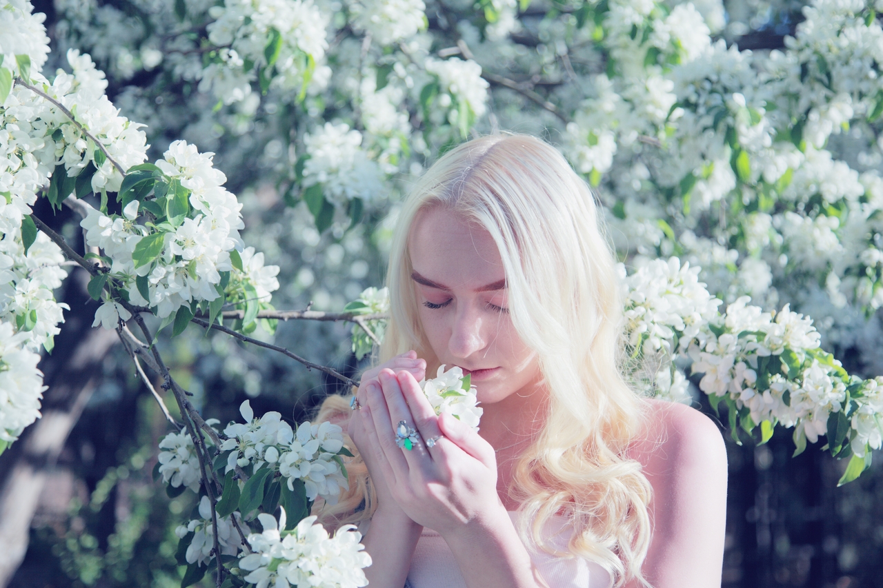 Woman holding a tree branch closer, gently cradling a flower between her hands to smell it.